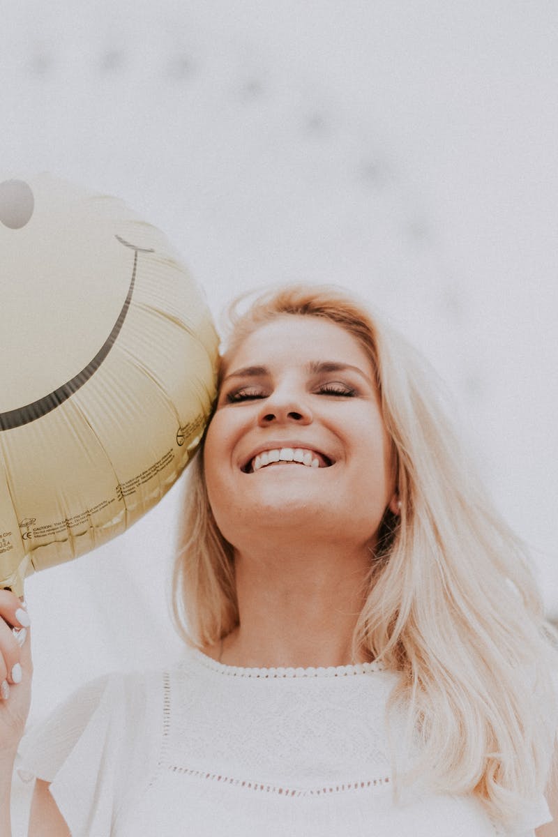 Cheerful woman holding a smiley balloon outdoors on a sunny day, exuding happiness and positivity.