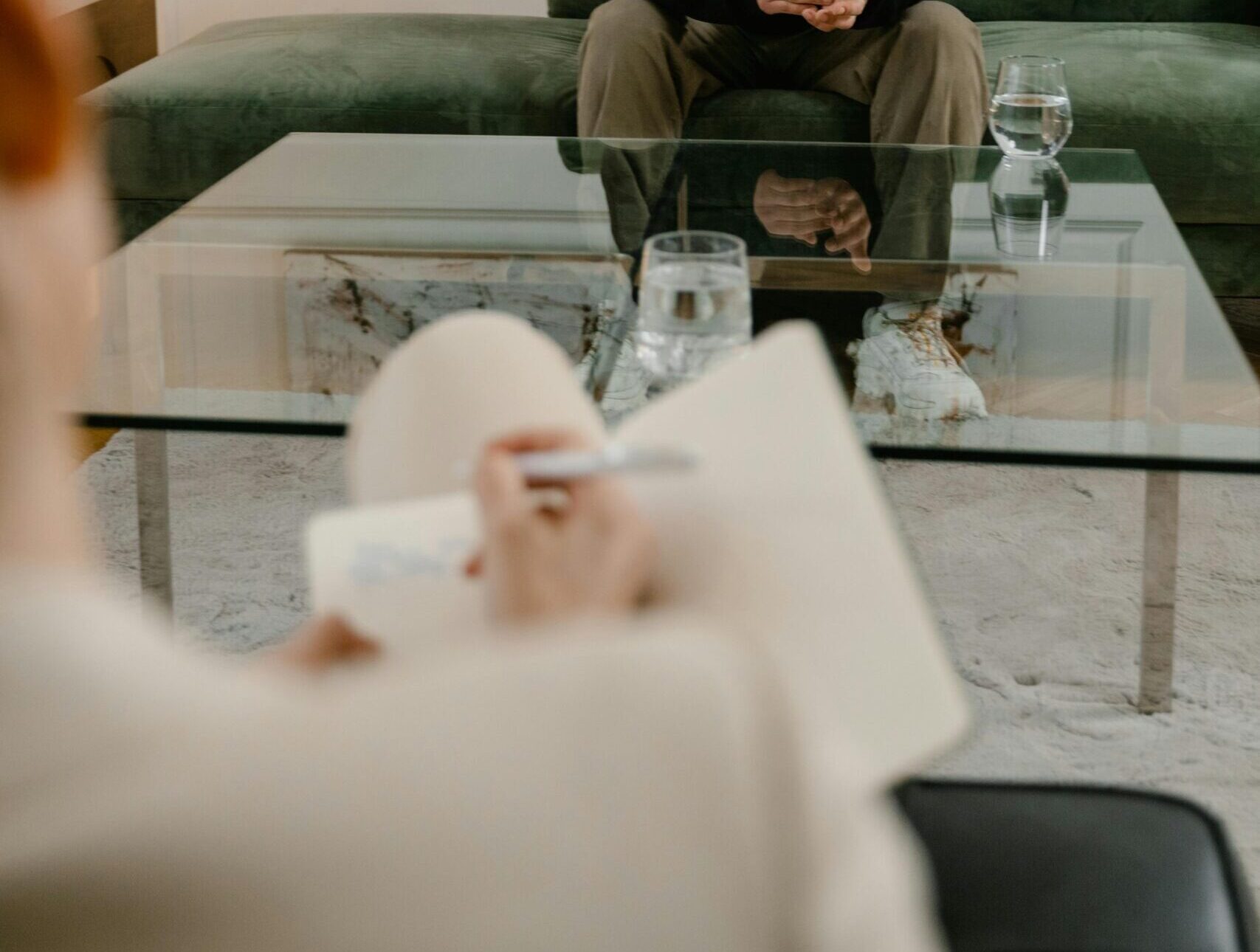 A man in a black hoodie sits on a couch, attending a therapy session indoors.